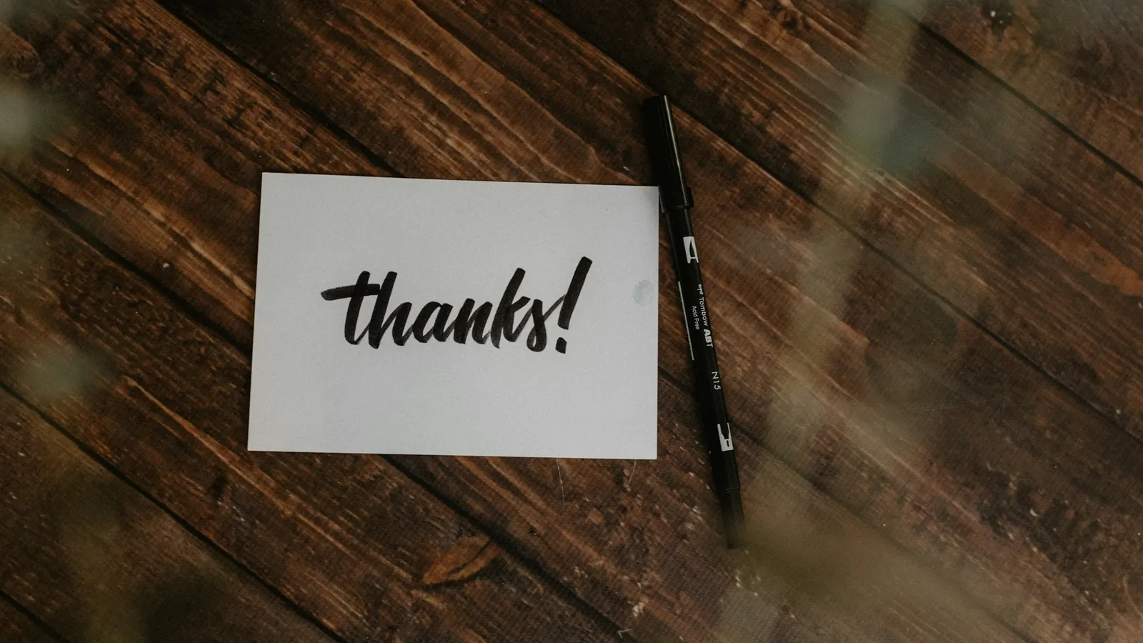 A handwritten thanks note and a pen on a wooden surface