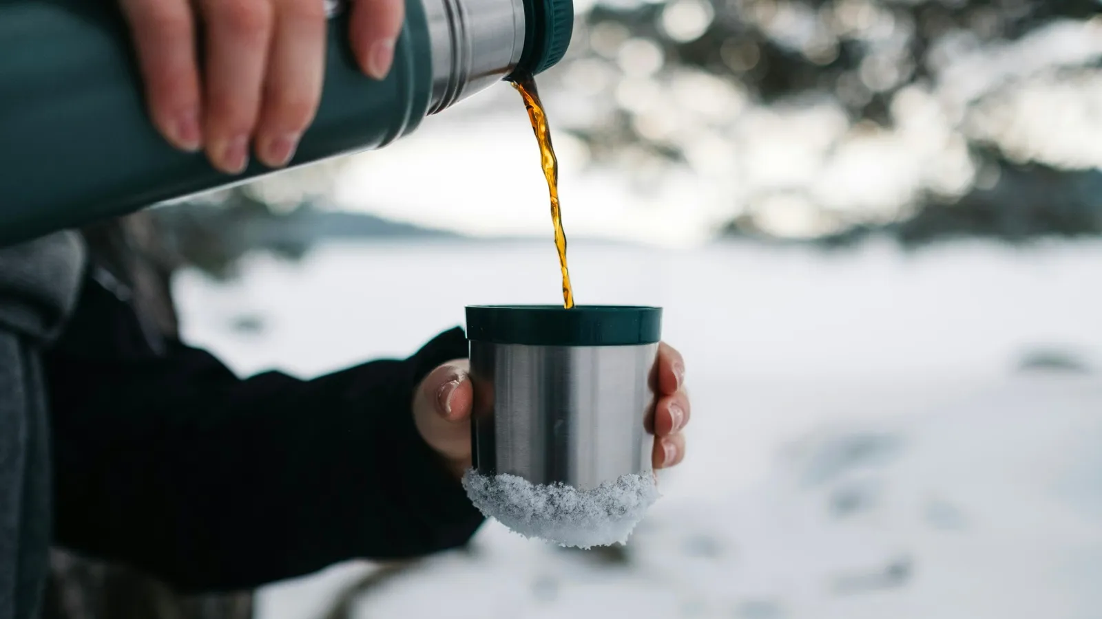 A hot drink poured from an insulated flask outdoors in snow