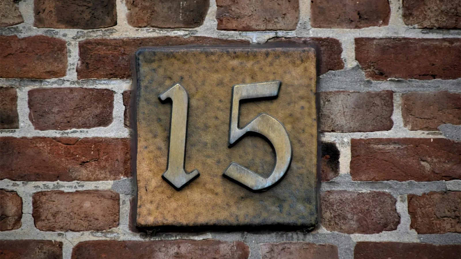A house number plate reading 15 on a brick wall