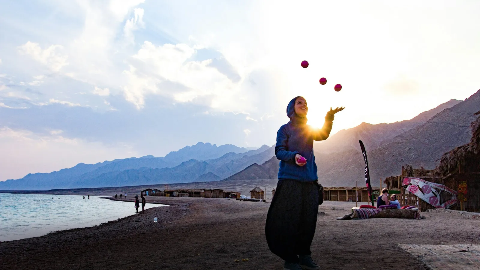 A juggler tossing balls into the air by the sea