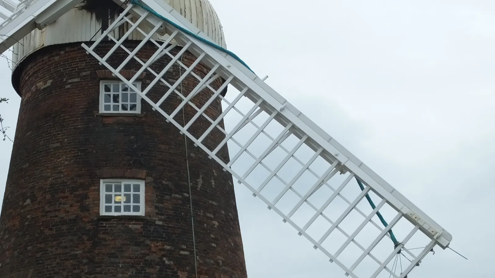 A large brick tower windmill with four white sails against a bright blue sky.