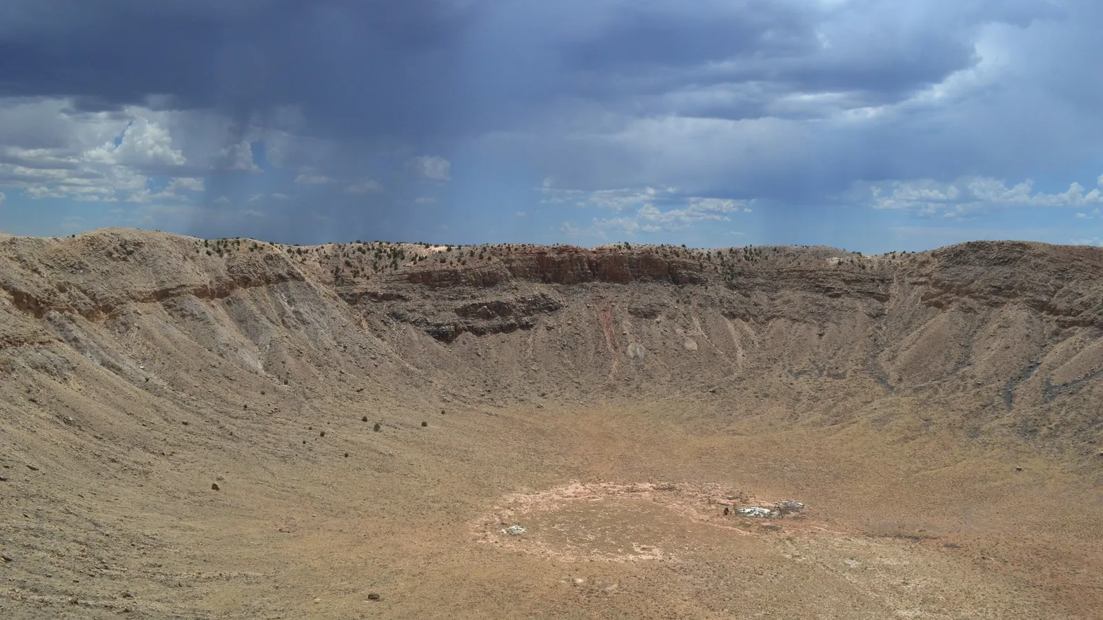 A large meteor crater in a dry desert under clouds