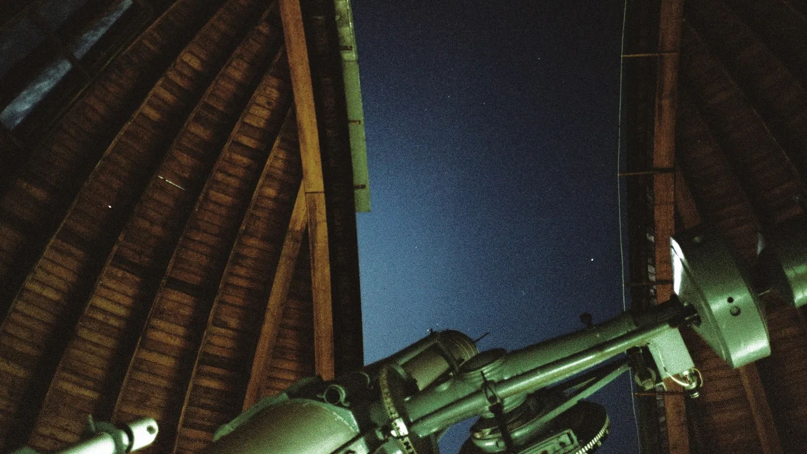 A large telescope pointing out of an observatory dome at night
