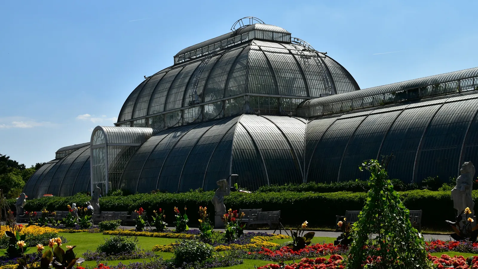 A large Victorian glasshouse behind formal flower beds