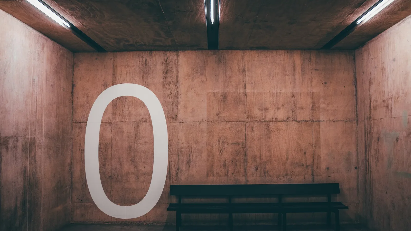 A large zero standing in an empty concrete room