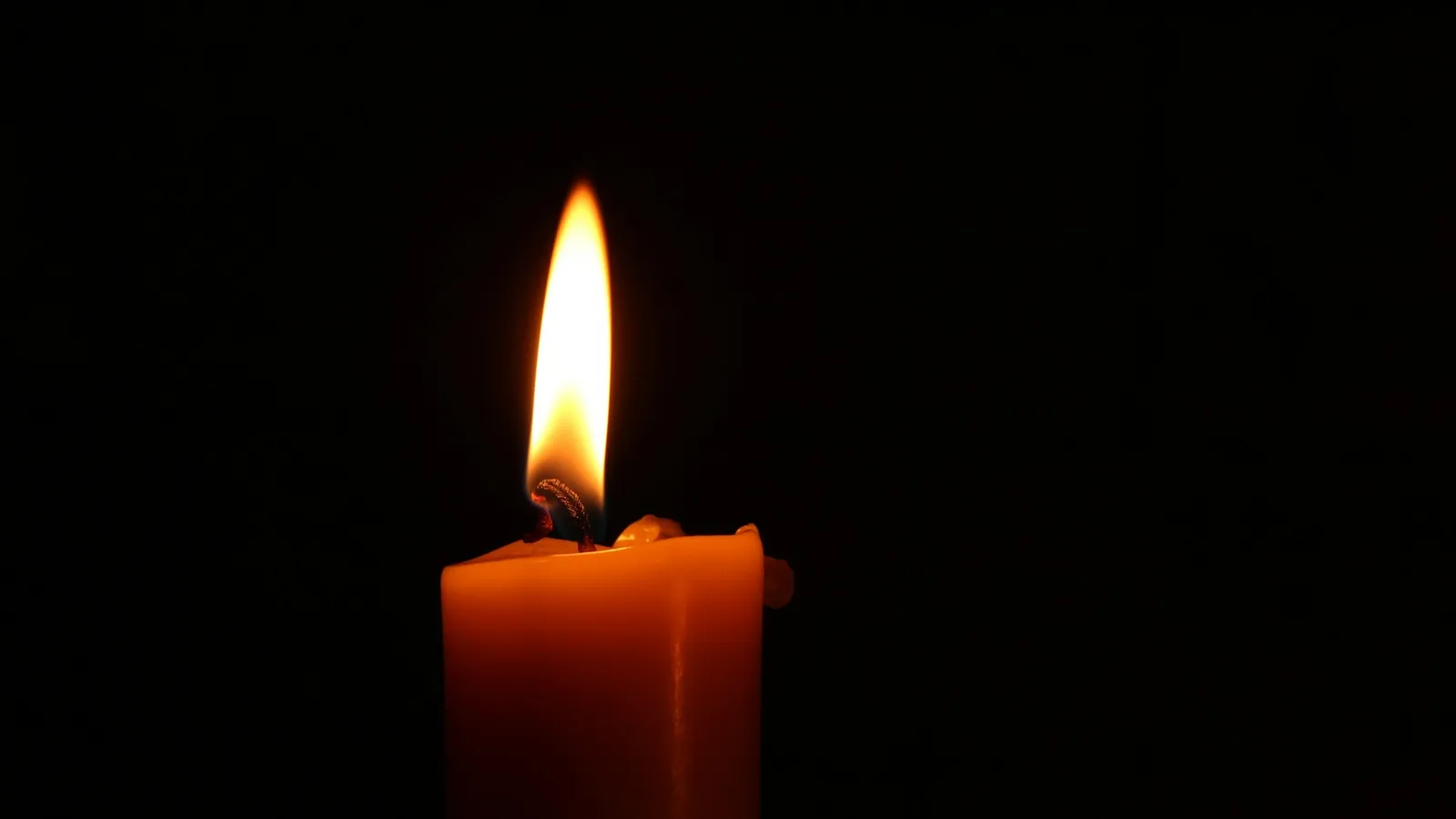 A lit red candle burning against a dark background