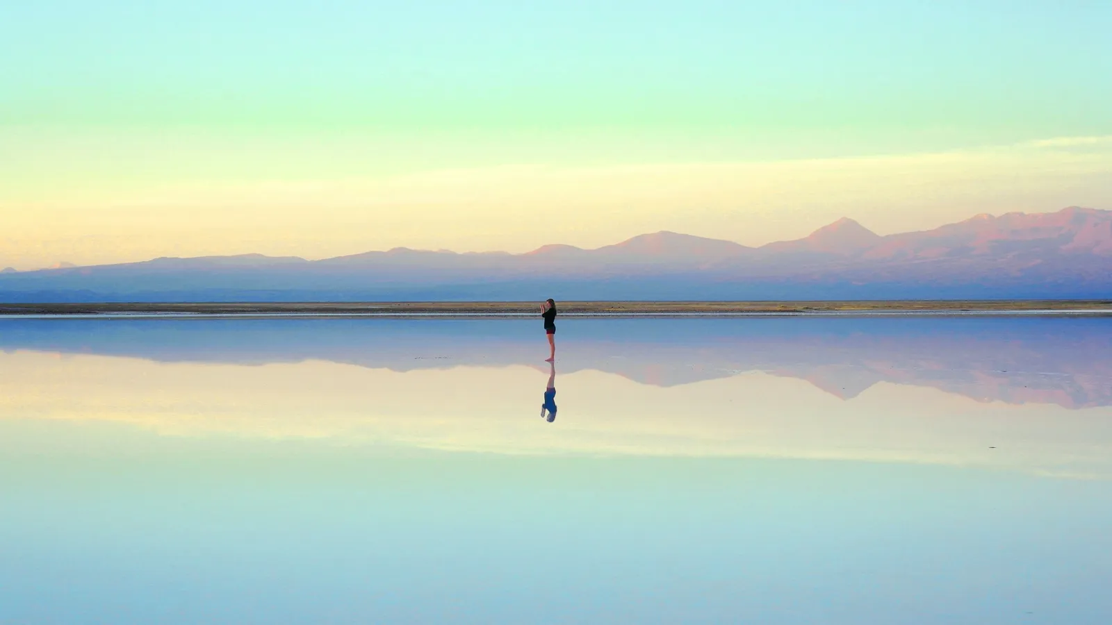 A lone figure and distant hills mirrored in a still lake