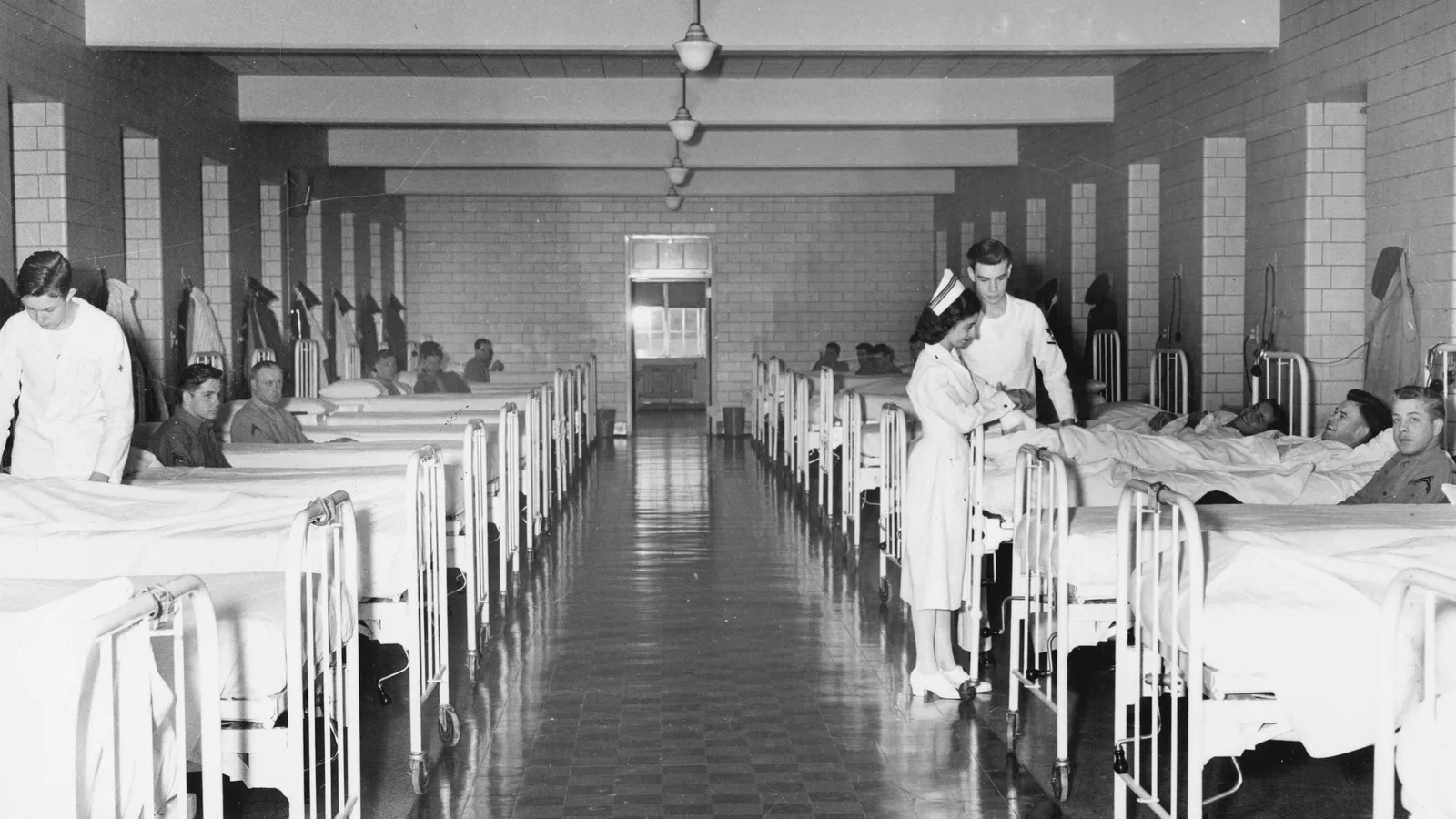 A long hospital ward lined with beds, in an old photograph
