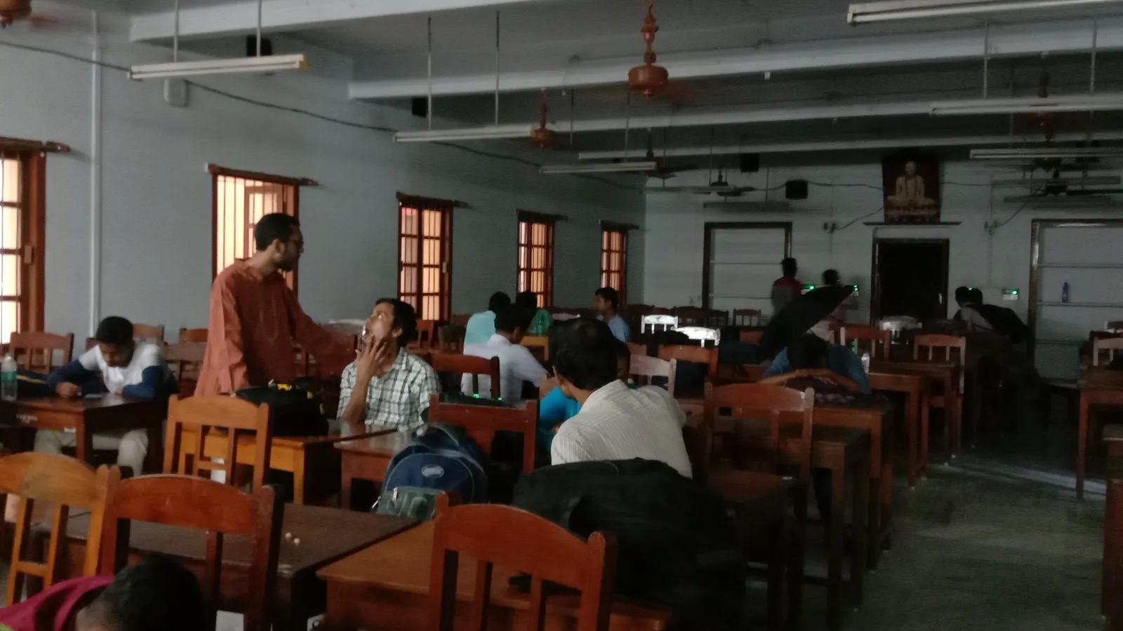 A man stands talking with a seated student in a college classroom in West Bengal