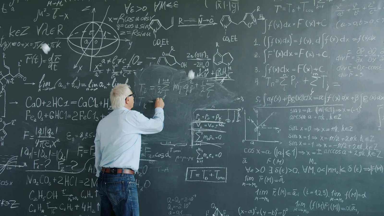 A man writing equations across a large blackboard