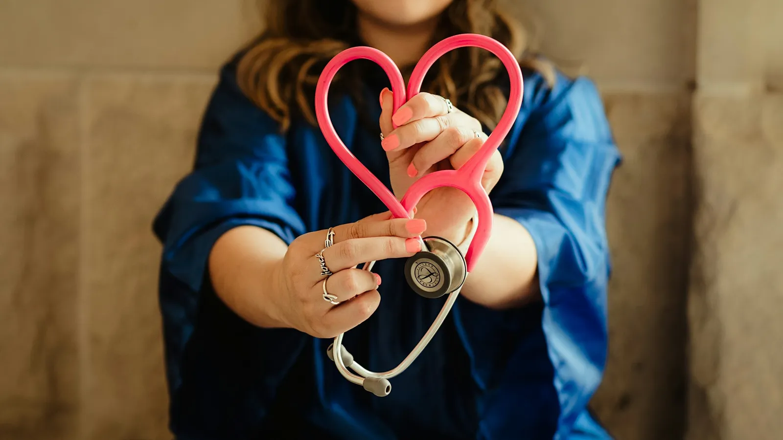 A medical student holding a heart-shaped stethoscope towards the camera