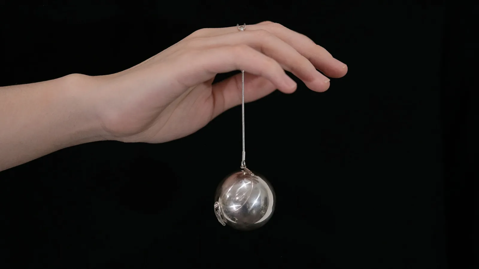 A metal ball hanging from a hand on a chain
