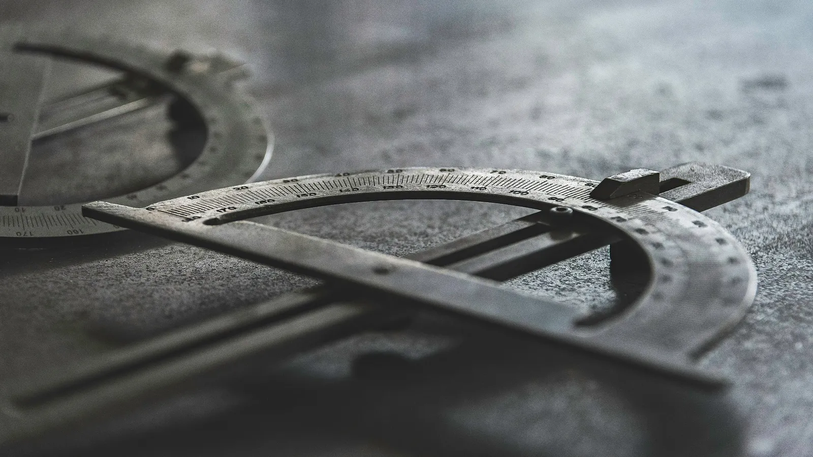 A metal protractor lying on a grey surface in low light