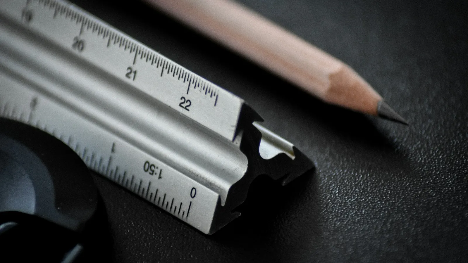A metal ruler and a sharpened pencil on a dark desk