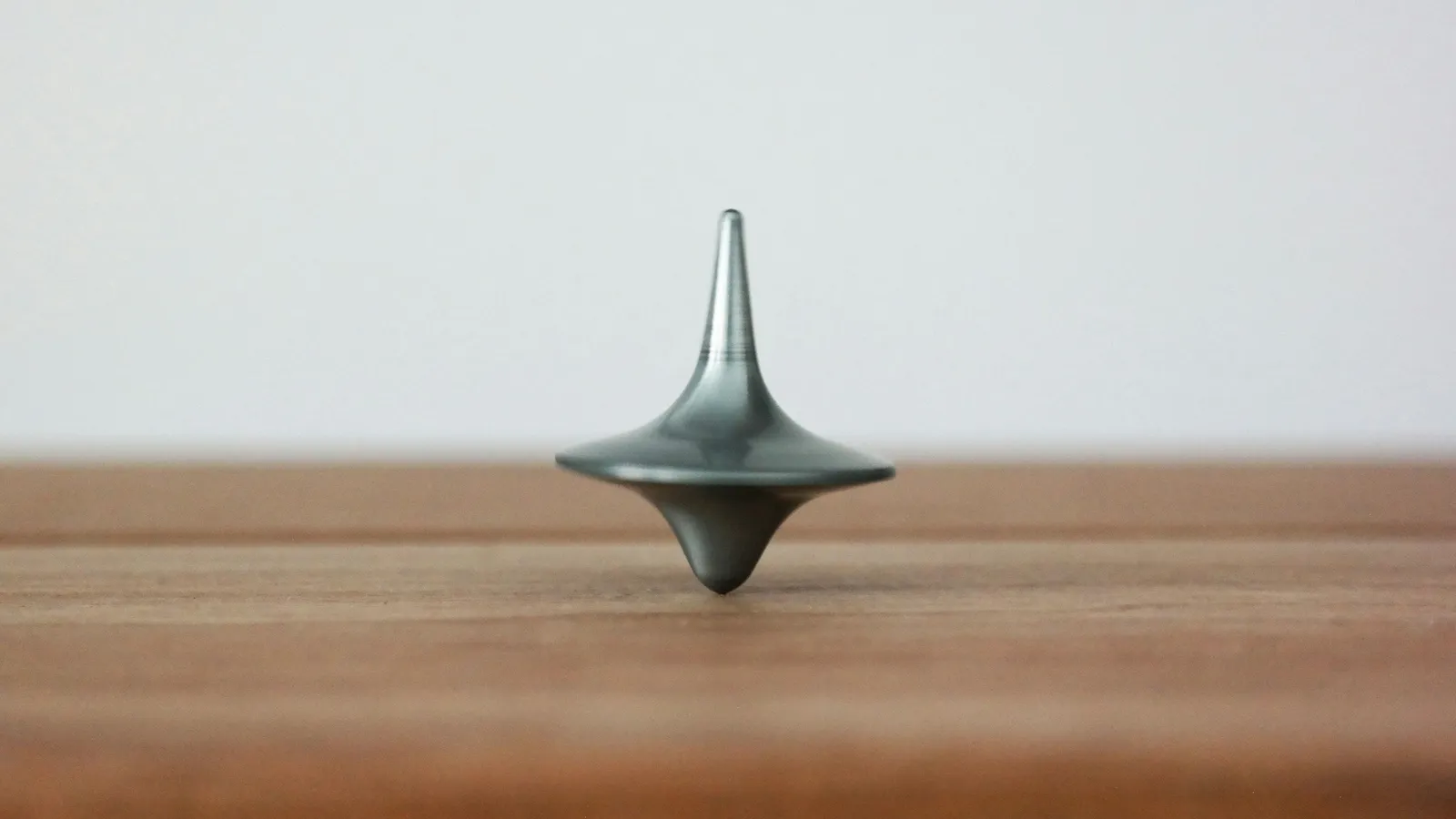 A metal spinning top balanced on its tip on a wooden table
