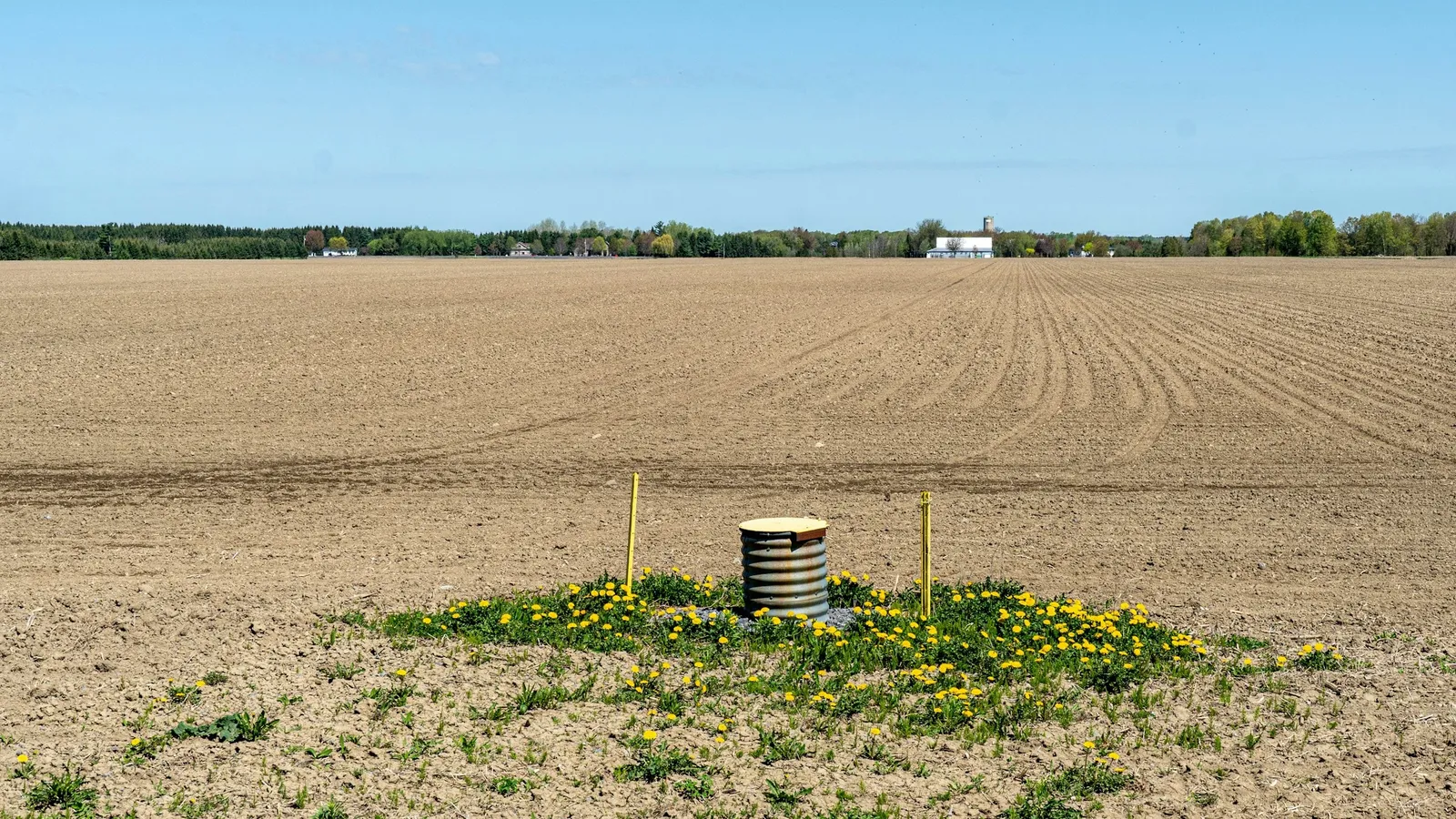 A metal well casing standing in a ploughed field