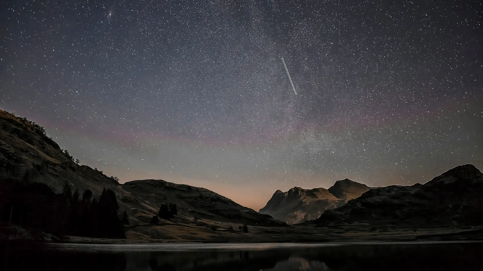 A meteor streak across a starry sky above mountains