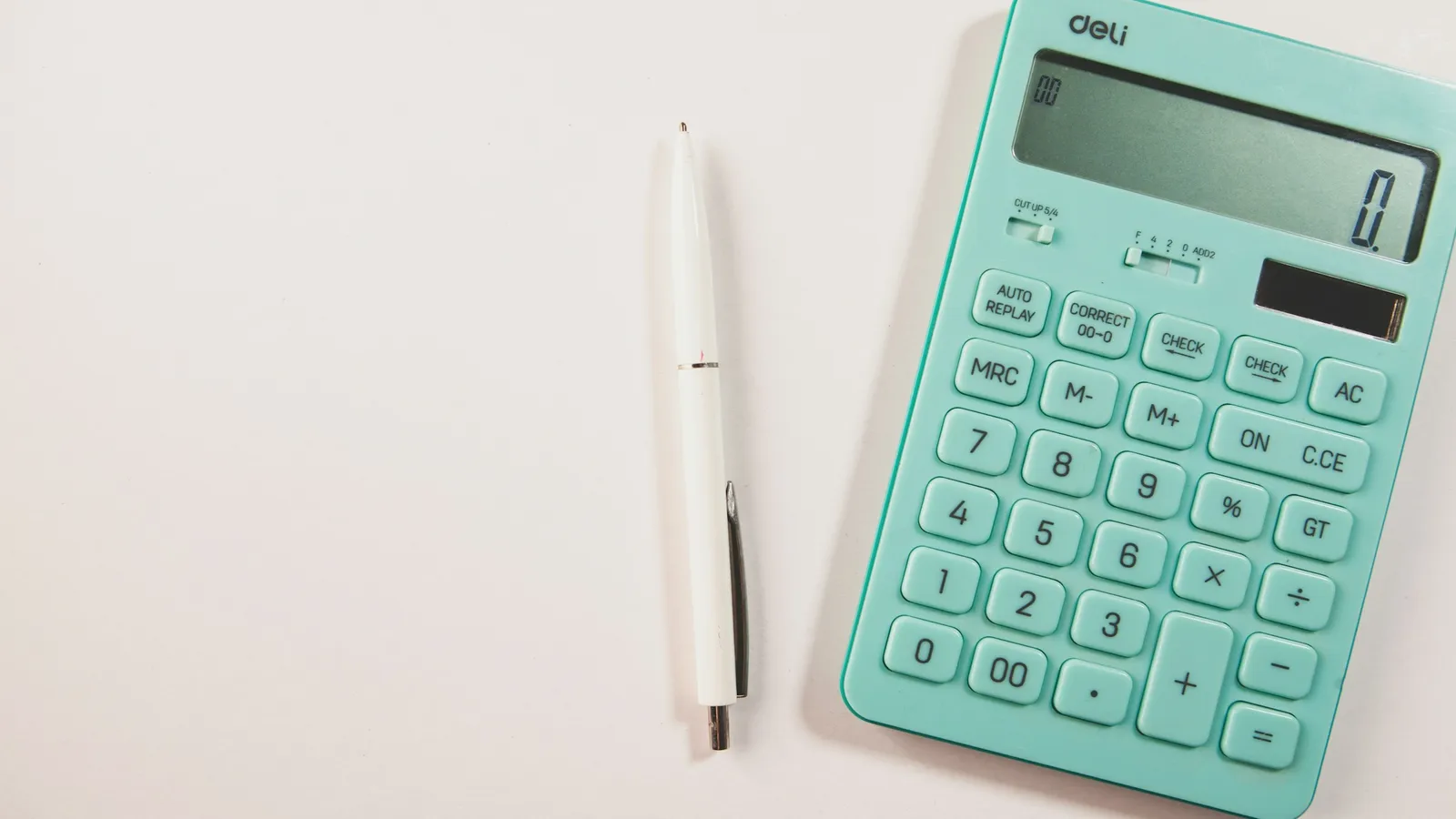 A mint-green calculator and a pen on a white desk
