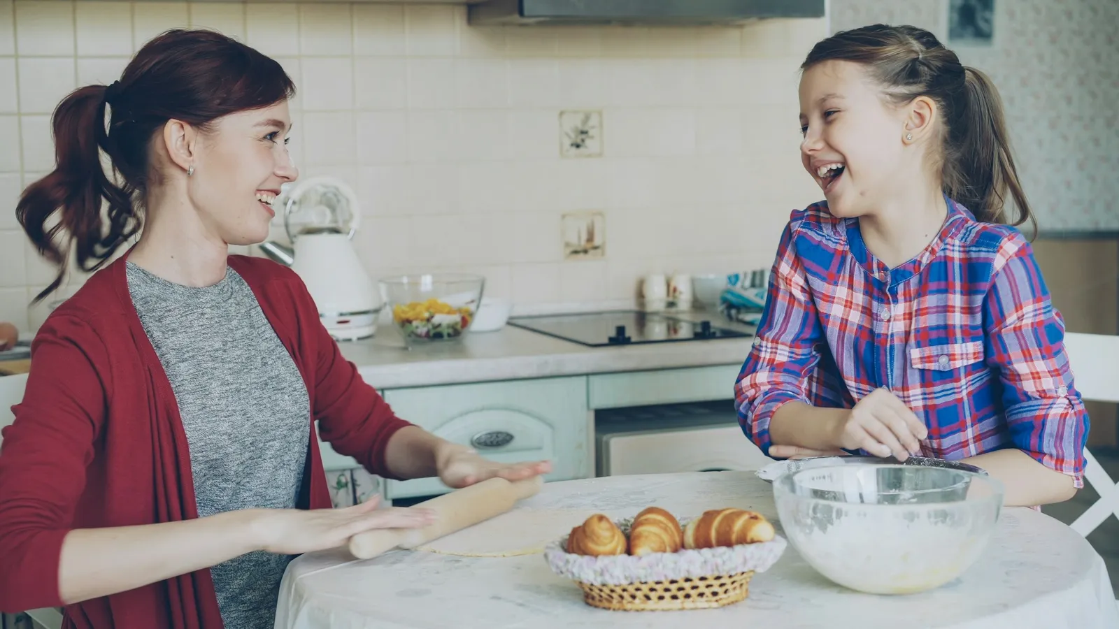 A mother and daughter laughing together while baking in the kitchen