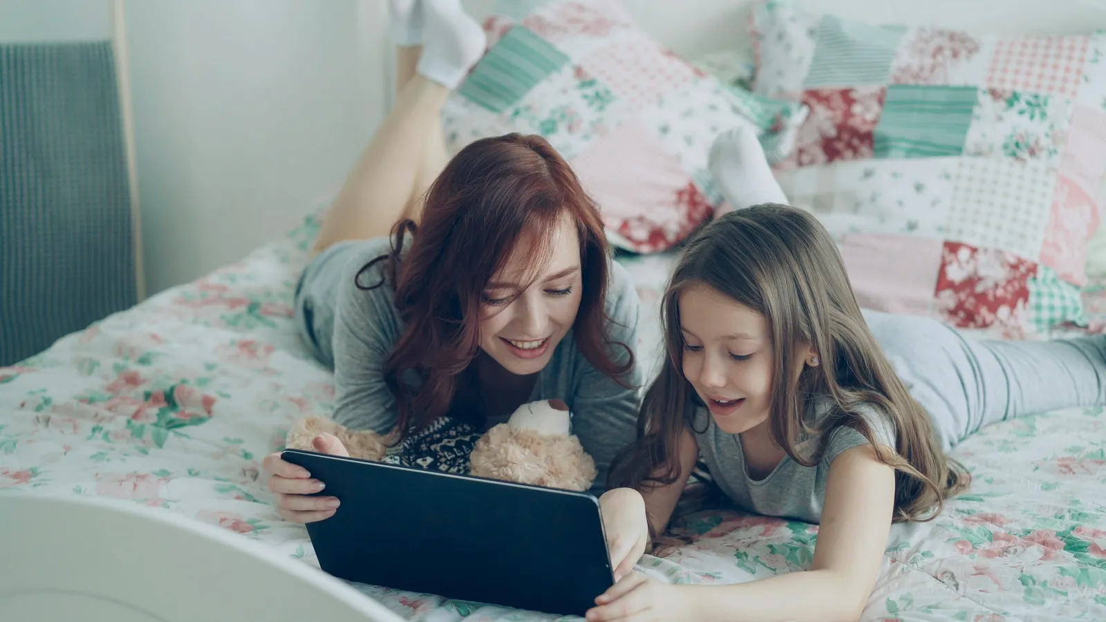 A mother and daughter watching a tablet together on a bed