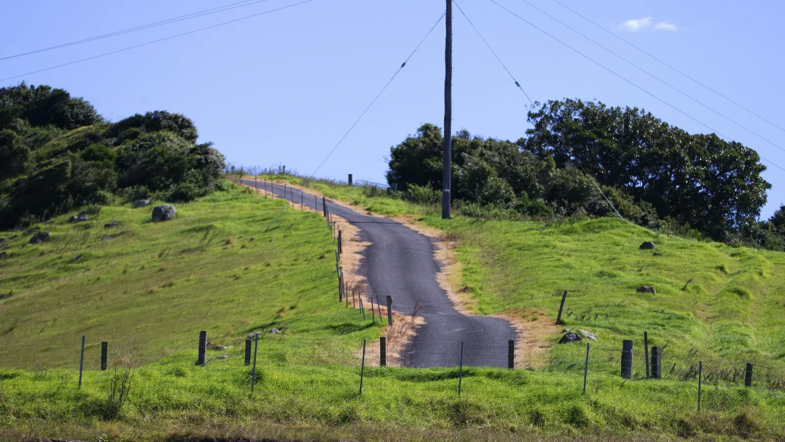 A narrow road rising and dipping over green hills