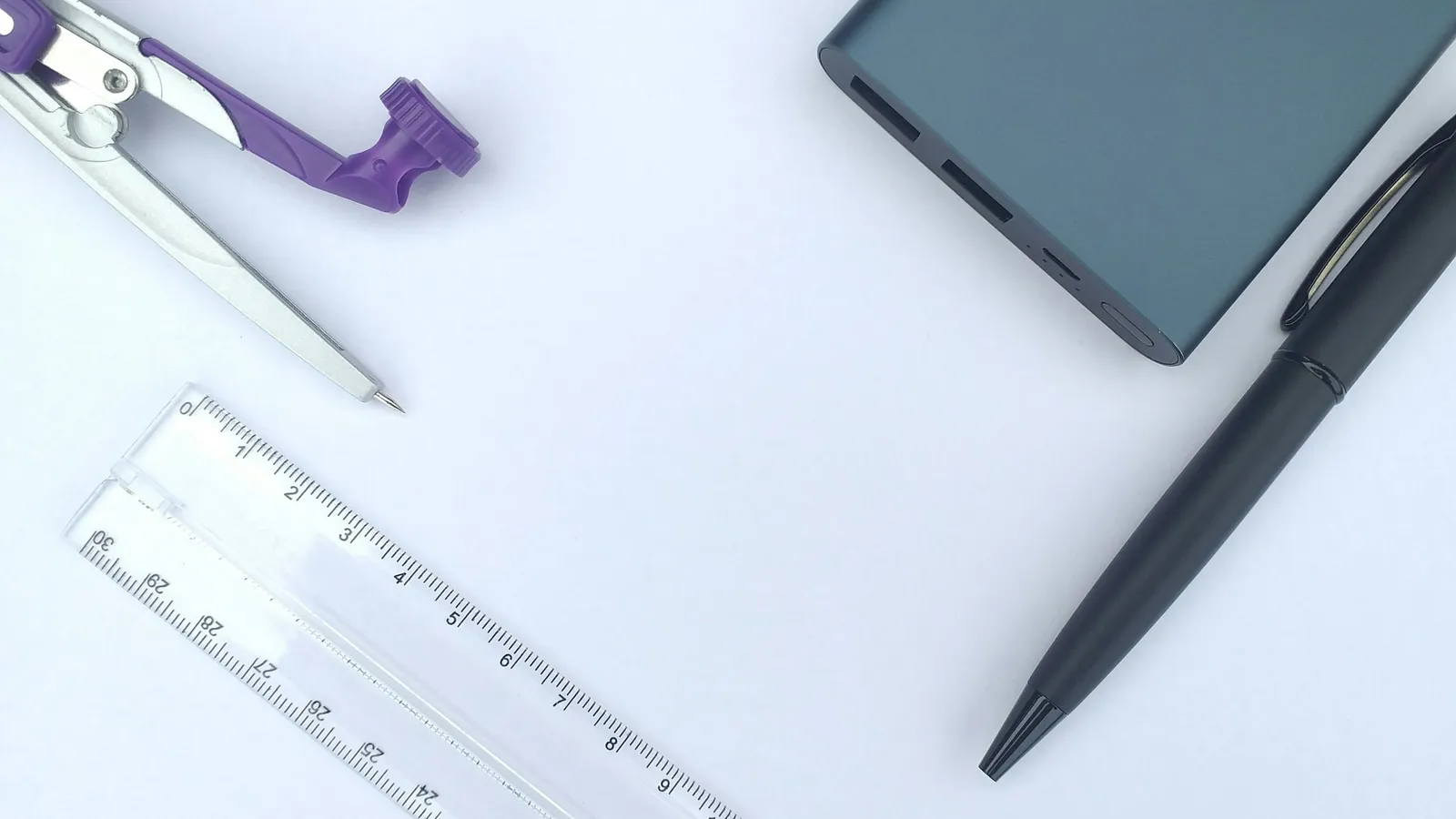 A pair of compasses, ruler and pen on a white desk