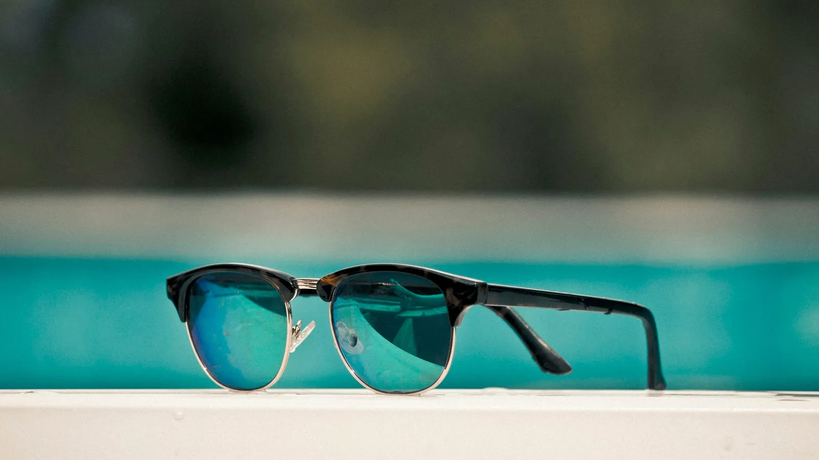 A pair of sunglasses beside a sunny pool