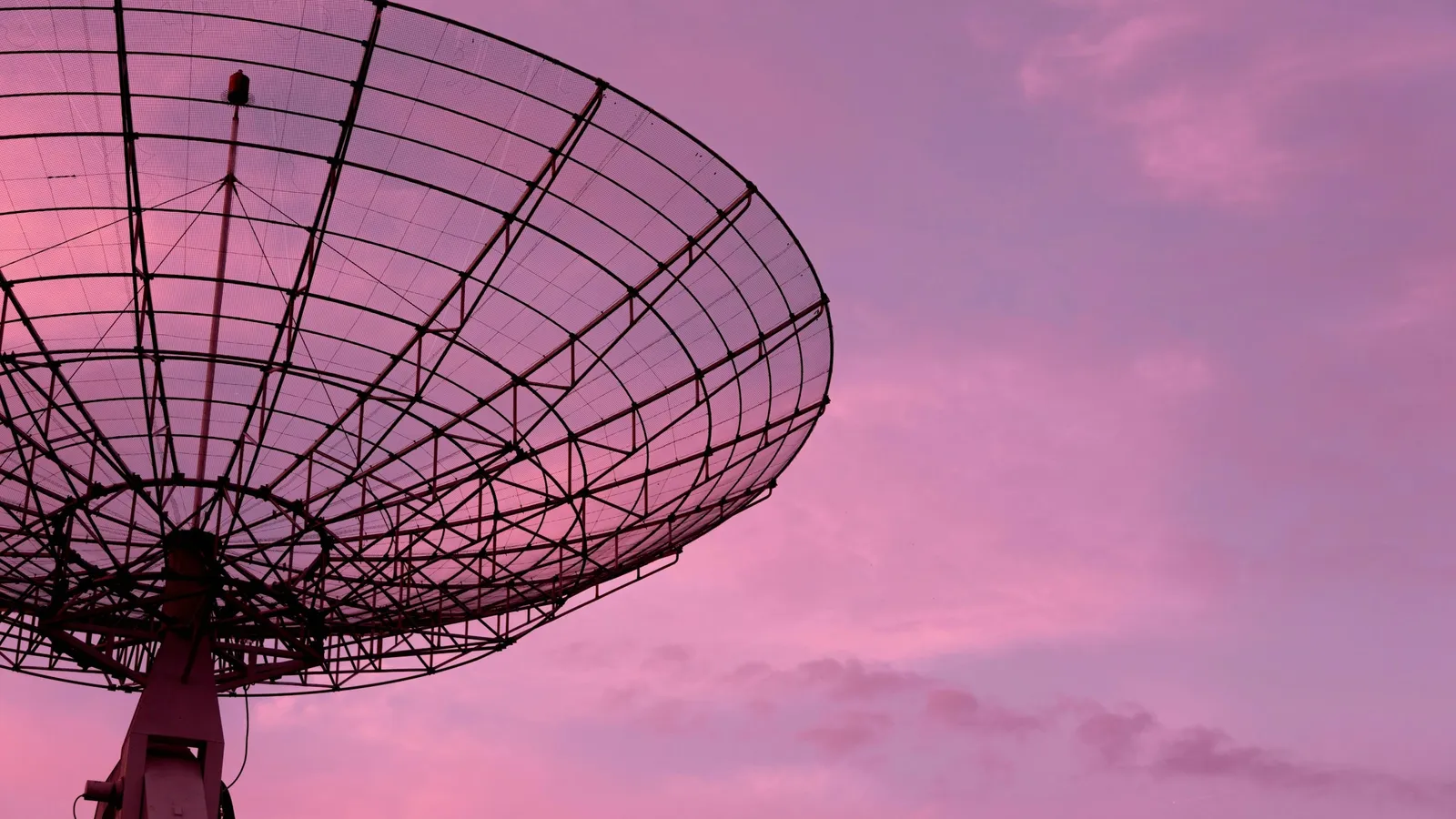 A parabolic dish antenna against a pink sky
