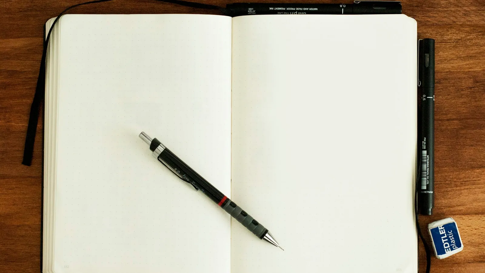 A pen resting on an open blank notebook on a wooden desk