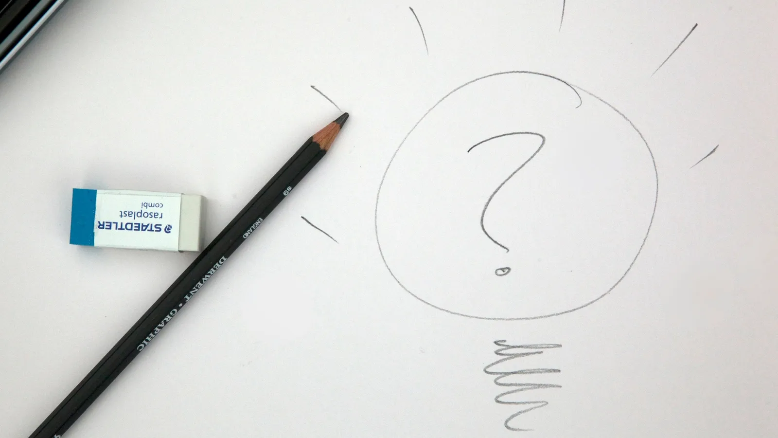 A pencil and eraser beside a question mark drawn on paper