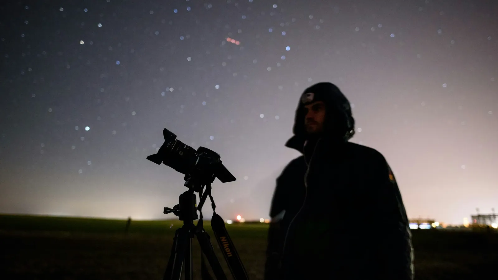 A person beside a telescope under a starry night sky