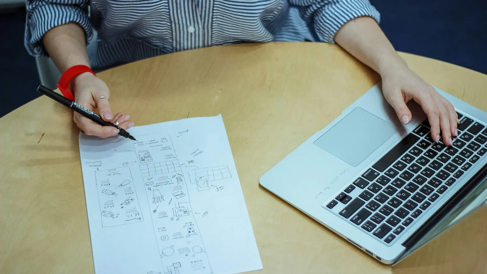 A person working through maths on paper beside an open laptop
