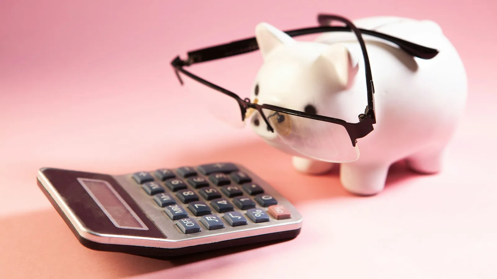 A piggy bank wearing glasses next to a calculator