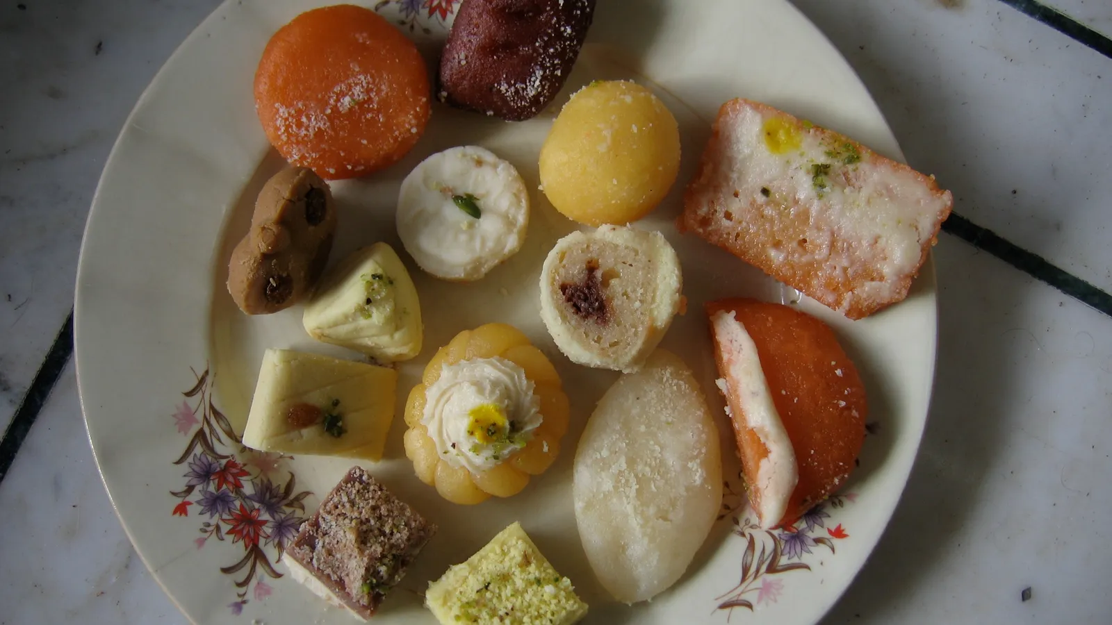 A plate of assorted Indian sweets on a white marble surface