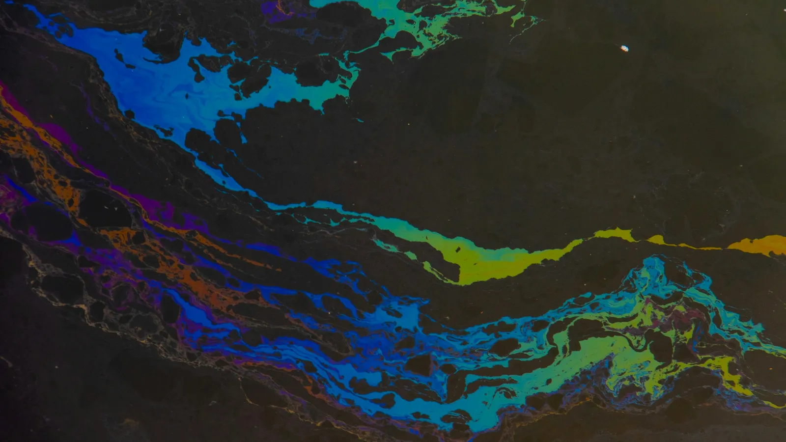 A rainbow sheen of oil spreading across a water surface