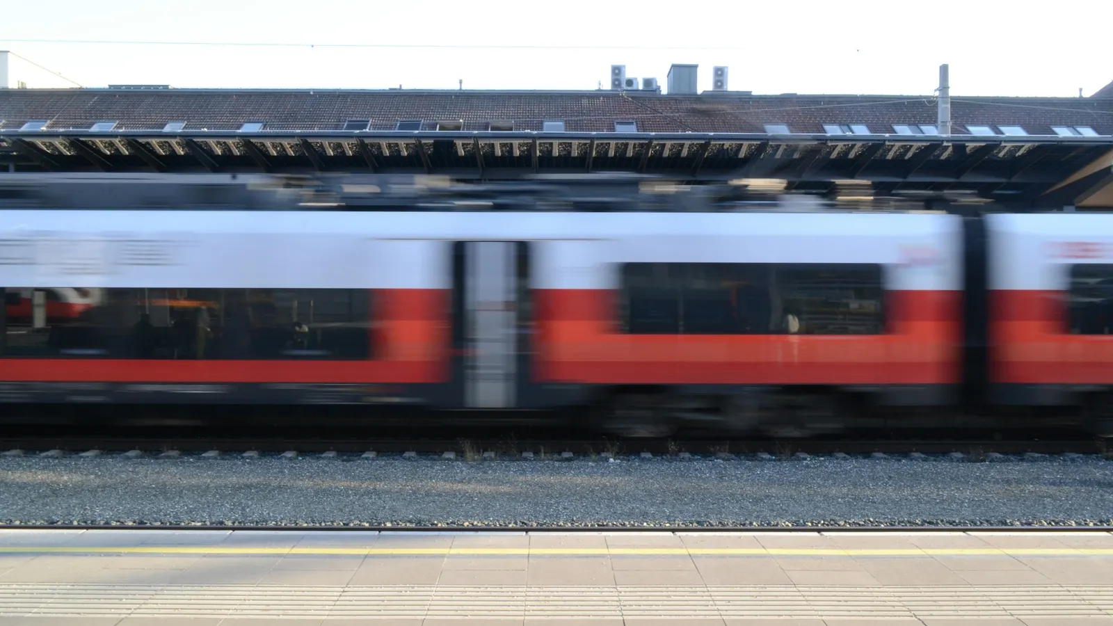 A red and white train moving fast past a station