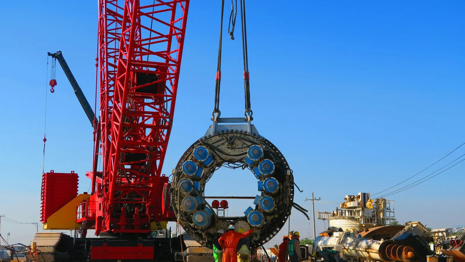 A red crane with a large round lifting magnet at a scrapyard