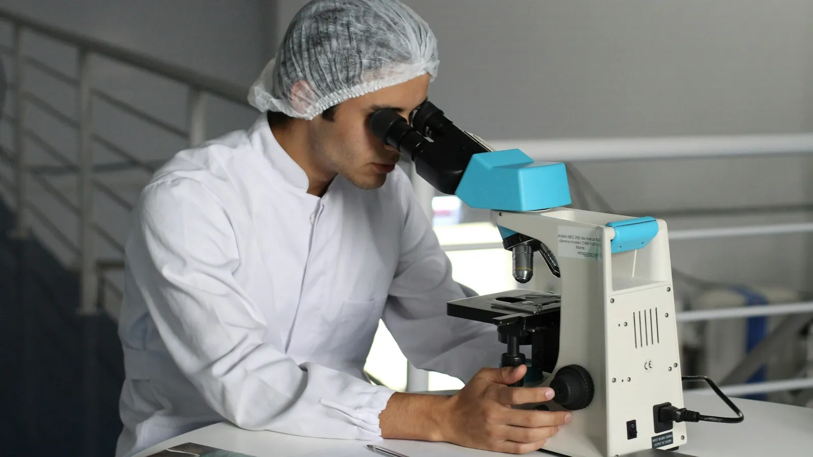 A researcher in a hairnet looking into a microscope in a laboratory
