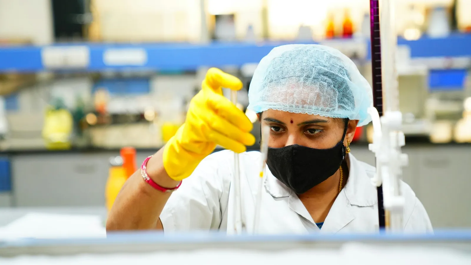 A researcher in gloves pipetting yellow liquid in a lab