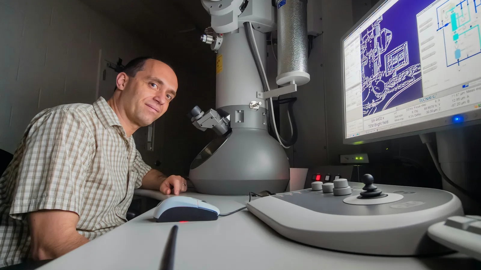 A researcher working at an electron microscope with images on a monitor