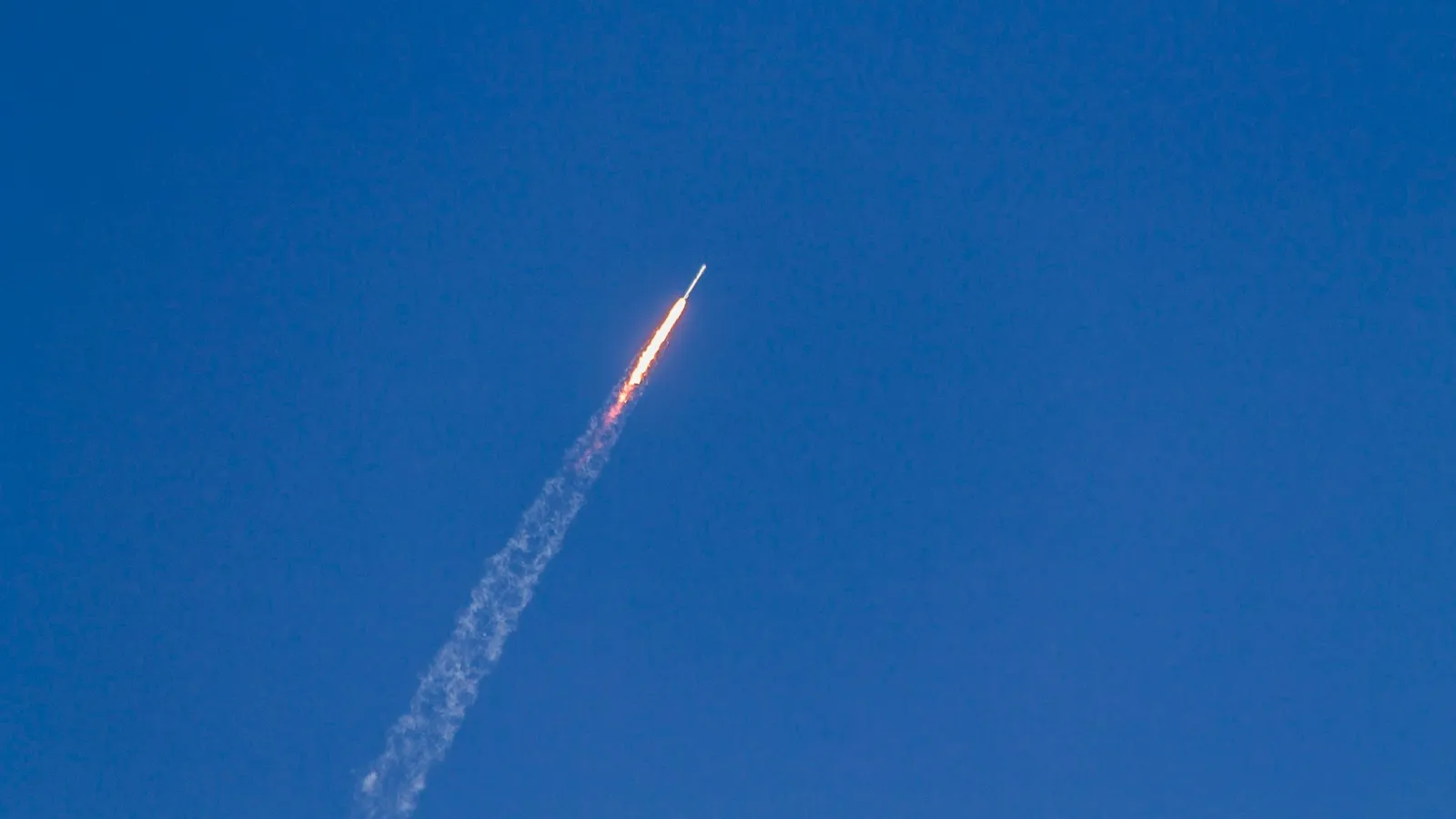 A rocket climbing into a clear blue sky trailing white smoke