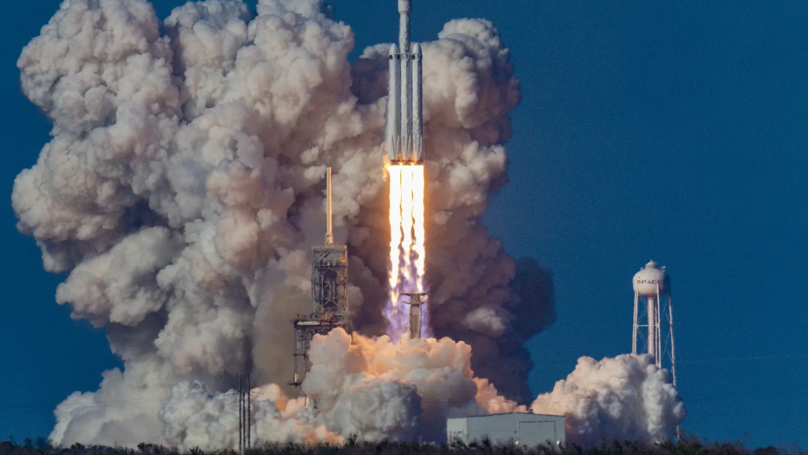 A rocket lifting off into a blue sky with a large plume of smoke