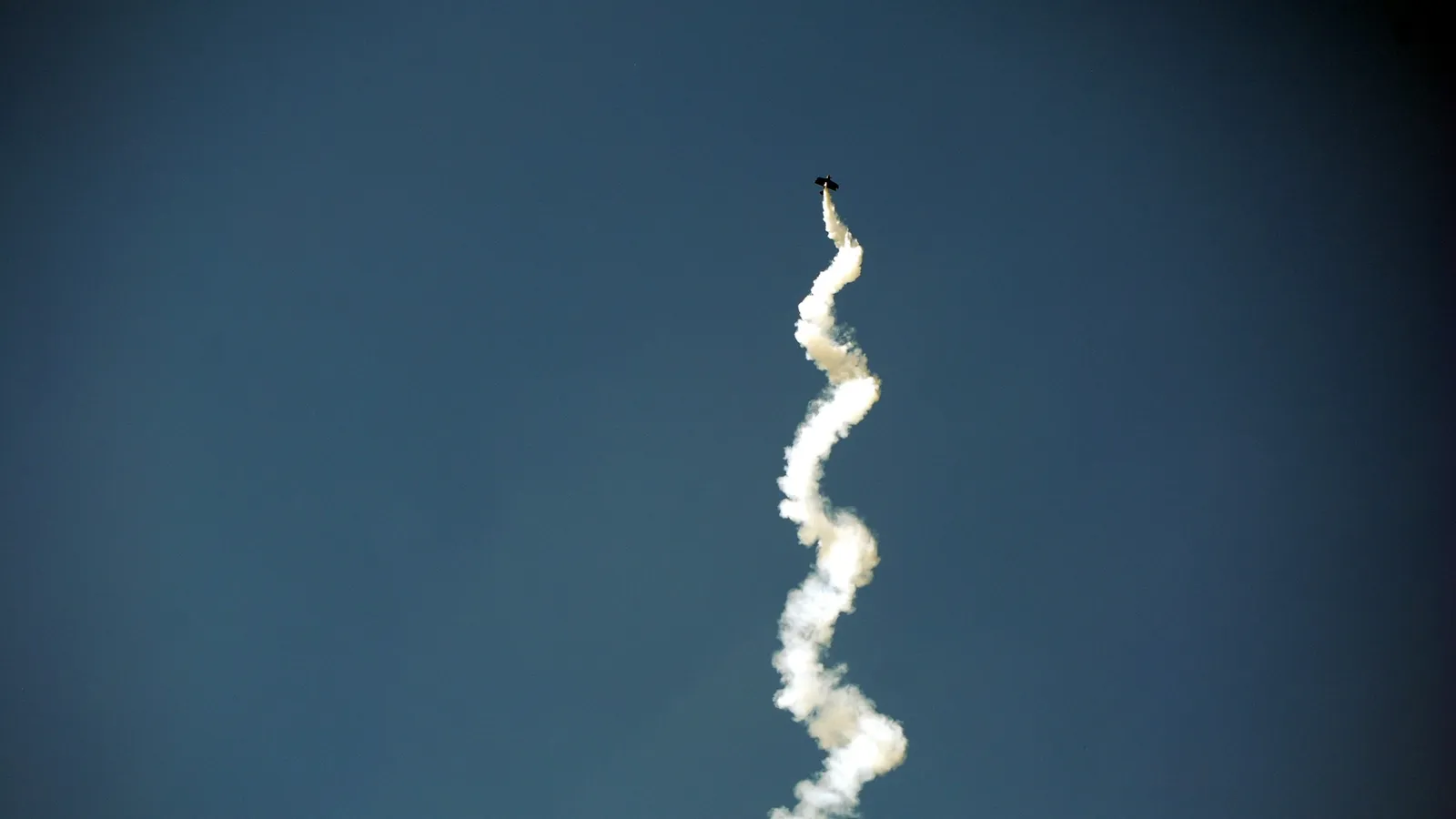 A rocket trail curving upward through a dark blue sky