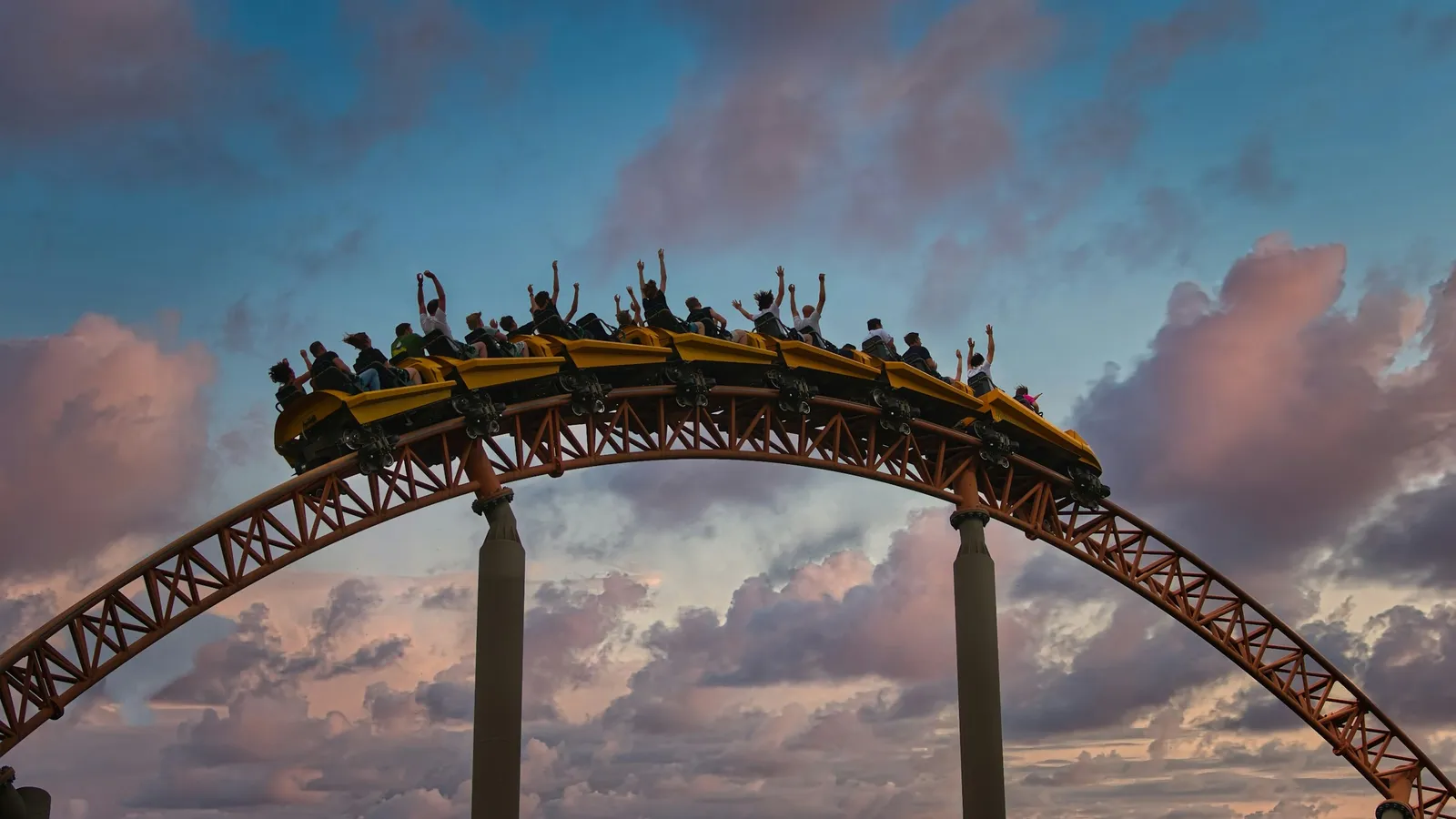 A roller coaster train cresting a curved hill at sunset