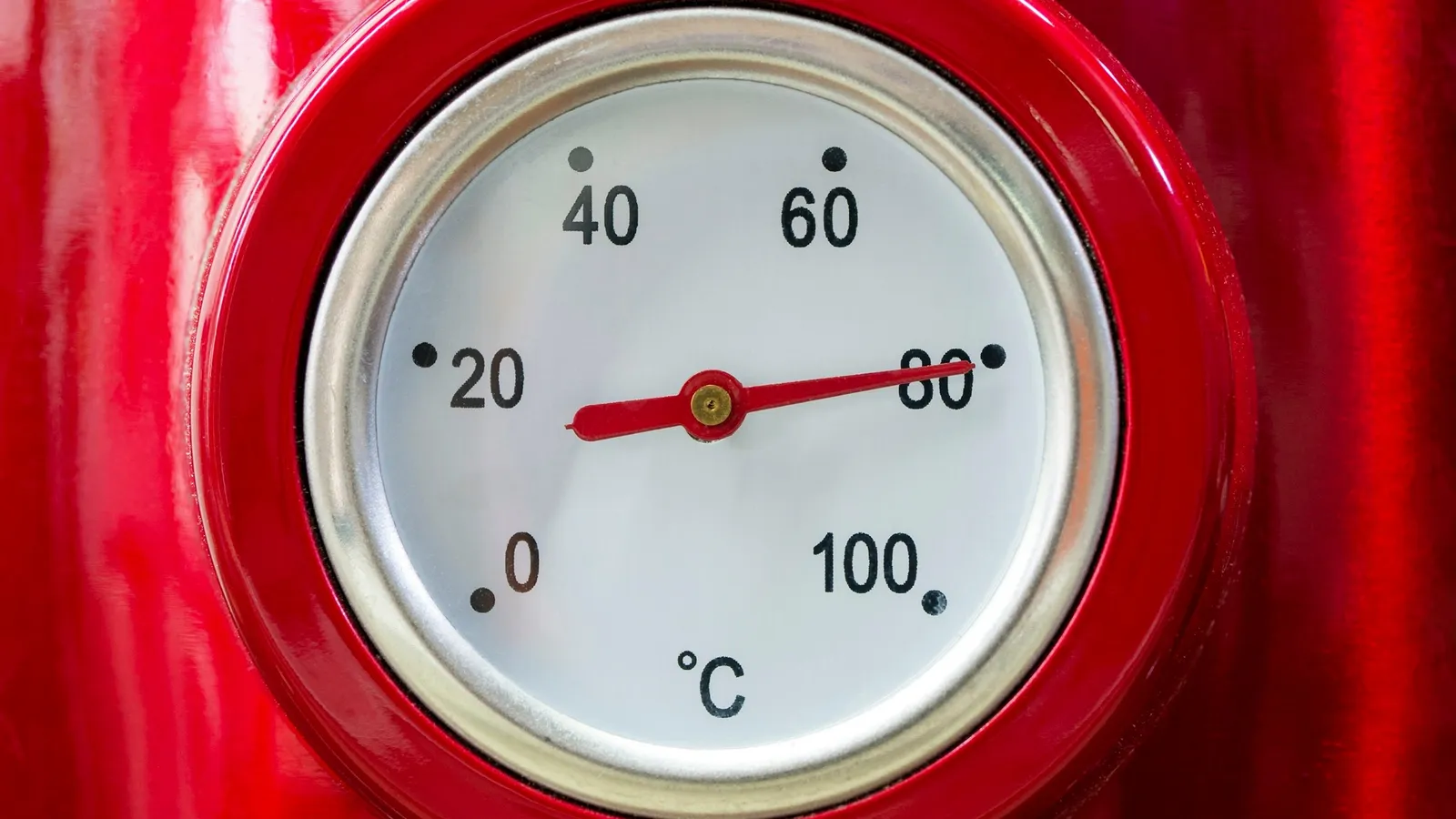 A round dial thermometer in Celsius on a red surface