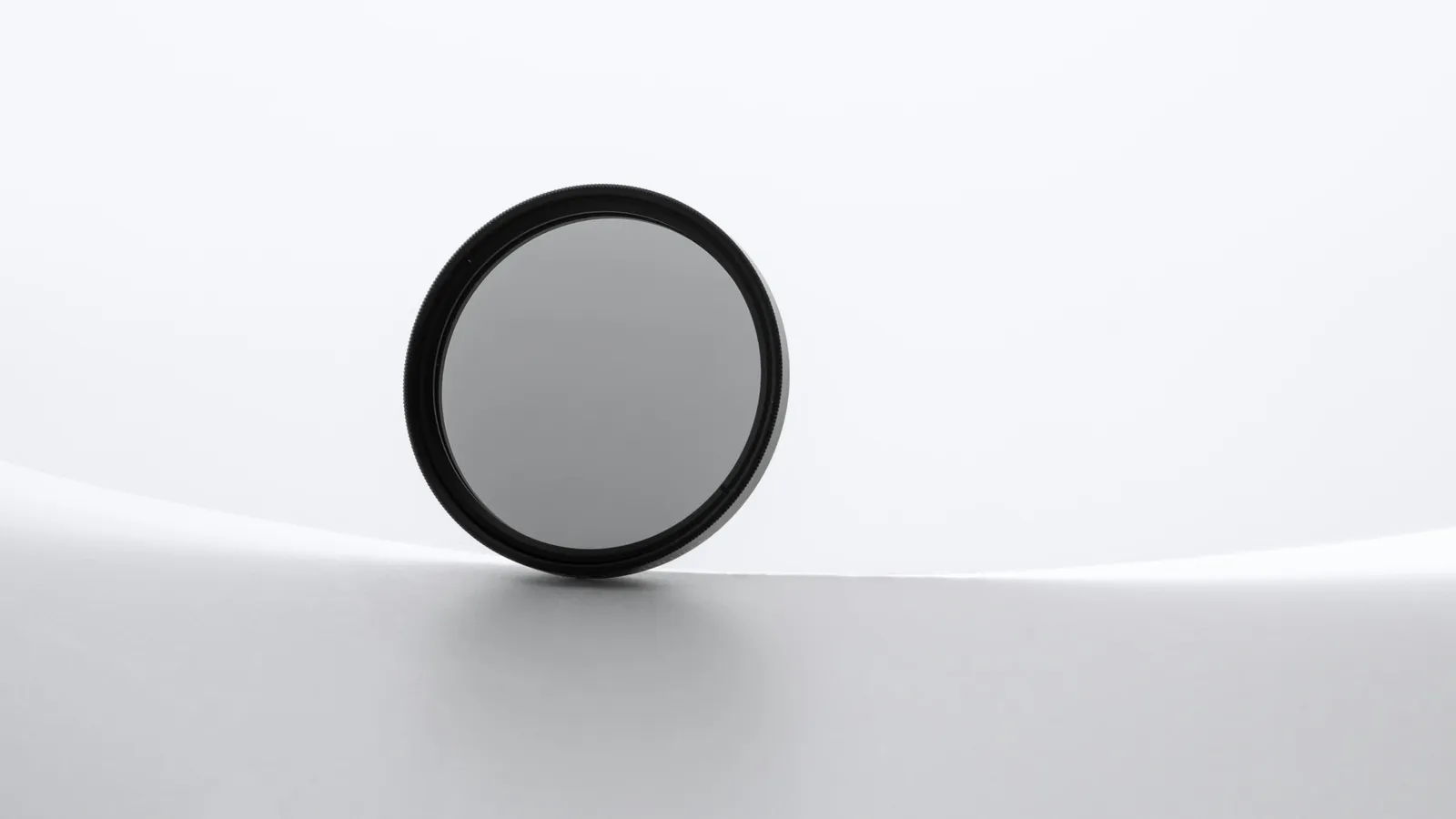 A round polarising filter standing on a white surface