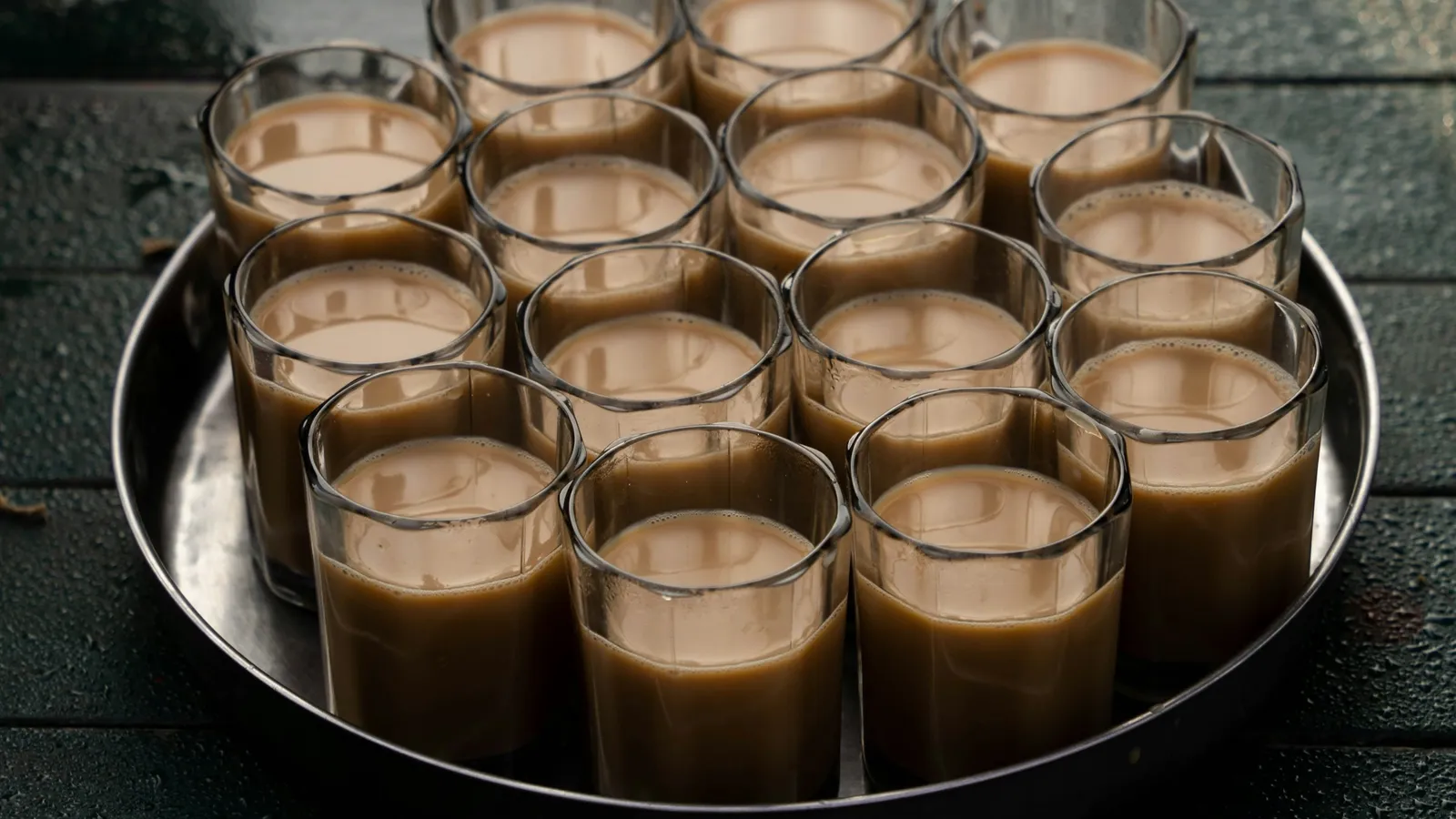 A round tray holding many small glasses of milky tea