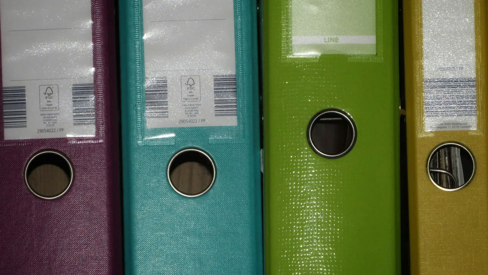 A row of coloured ring binders standing on a shelf