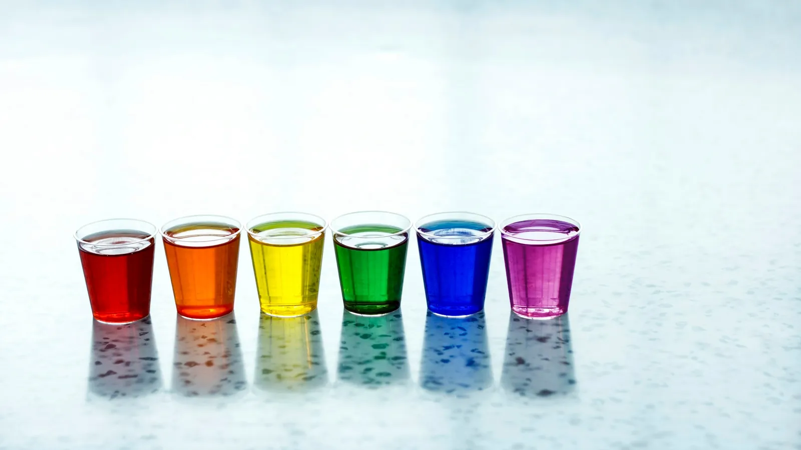 A row of glasses holding rainbow-coloured liquids