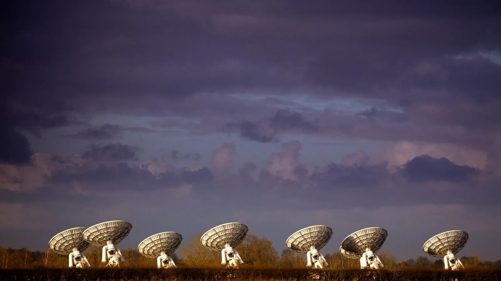 A row of radio telescope dishes under an evening sky